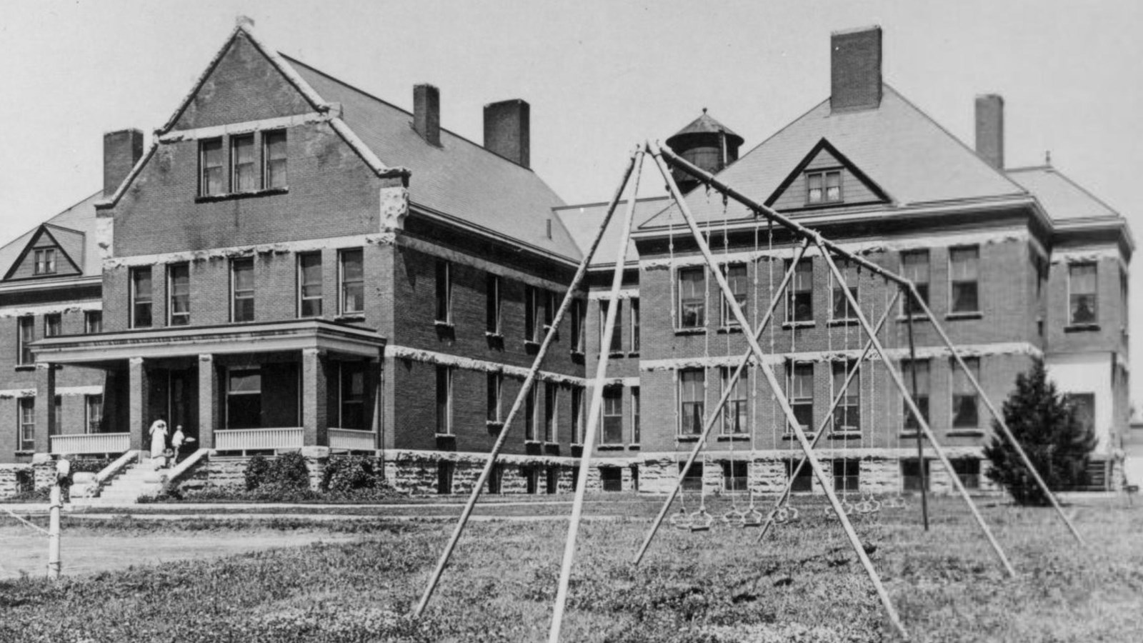 Large three-story building with two wings and dormers with a swing set in the foreground