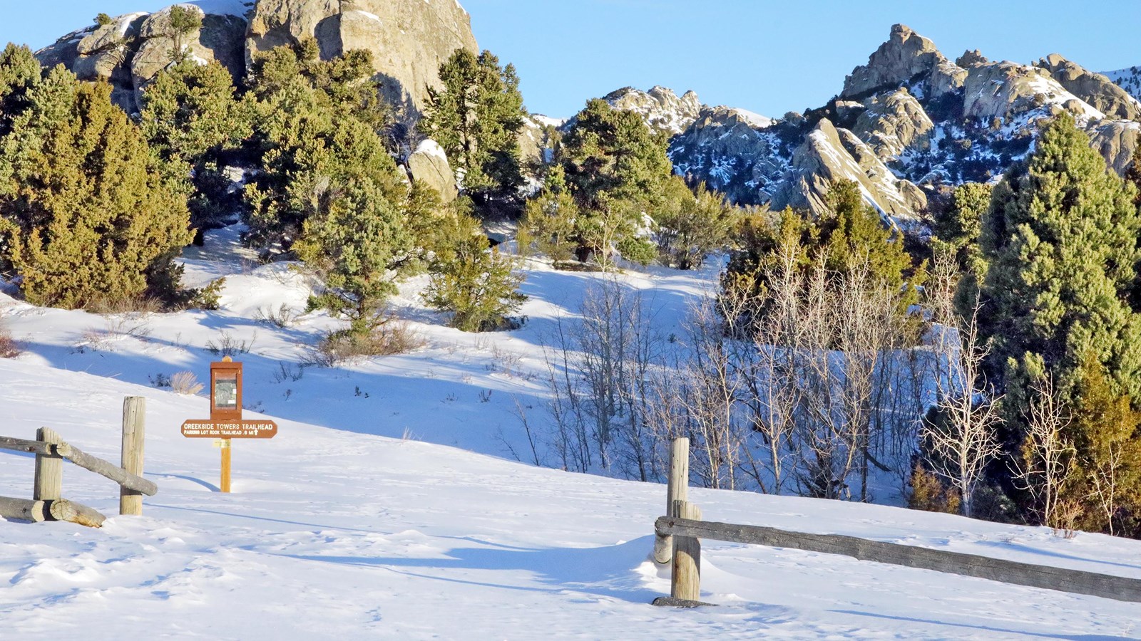 Creekside Trailhead sign over a foot of snow on the ground, granite formation in the backdrop.