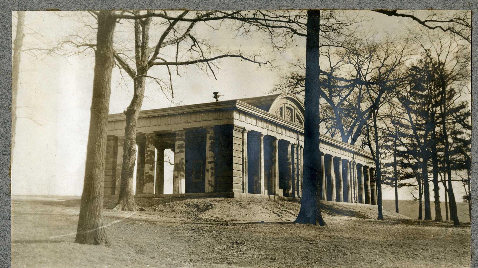 Black and white or large building on top of grassy hill with trees around it