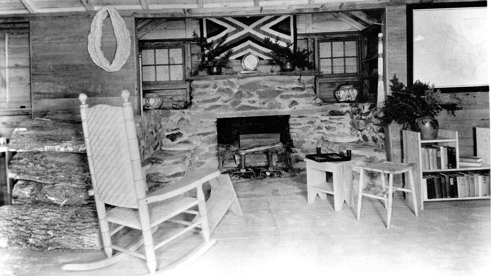 Black and white photo of rustic fireplace with a wooden rocking chair and plants in front.