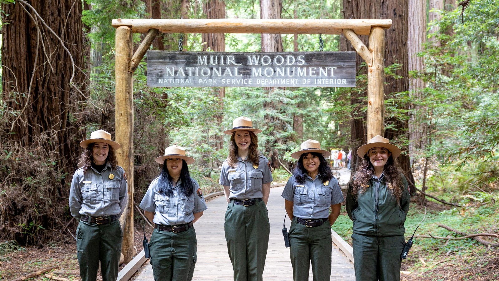 five rangers in uniform stand in front of the archway into Muir Woods