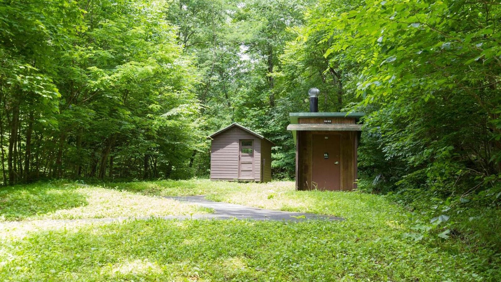 A small wooden, rectangular building surrounded by trees with a grass clearing in front of it.