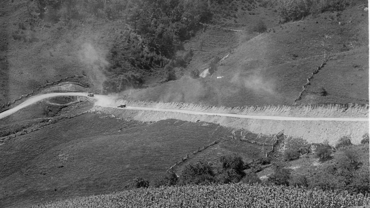 Original Rapidan Road snaking through the ridges. Two cars driving the road creating dust.