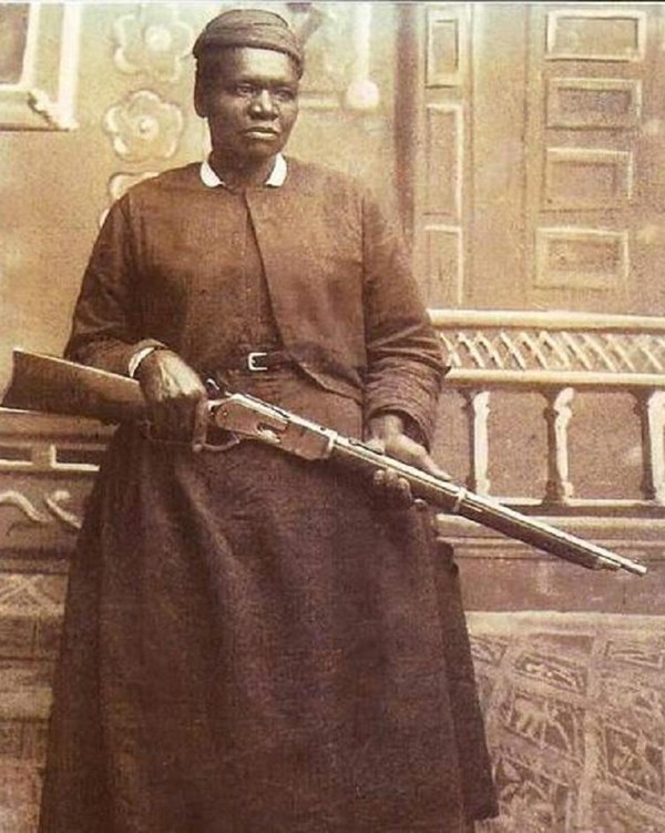 Woman holding a gun with a dog beside her. 
