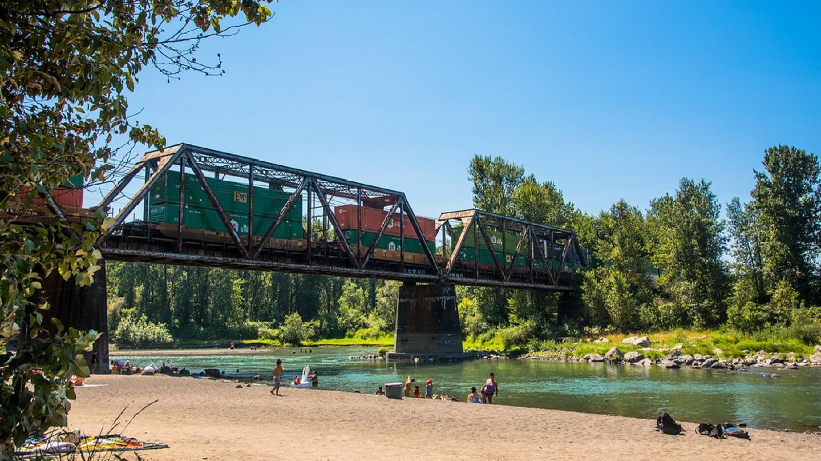 An old railway bridge stretches across a river while swimmers frolic below