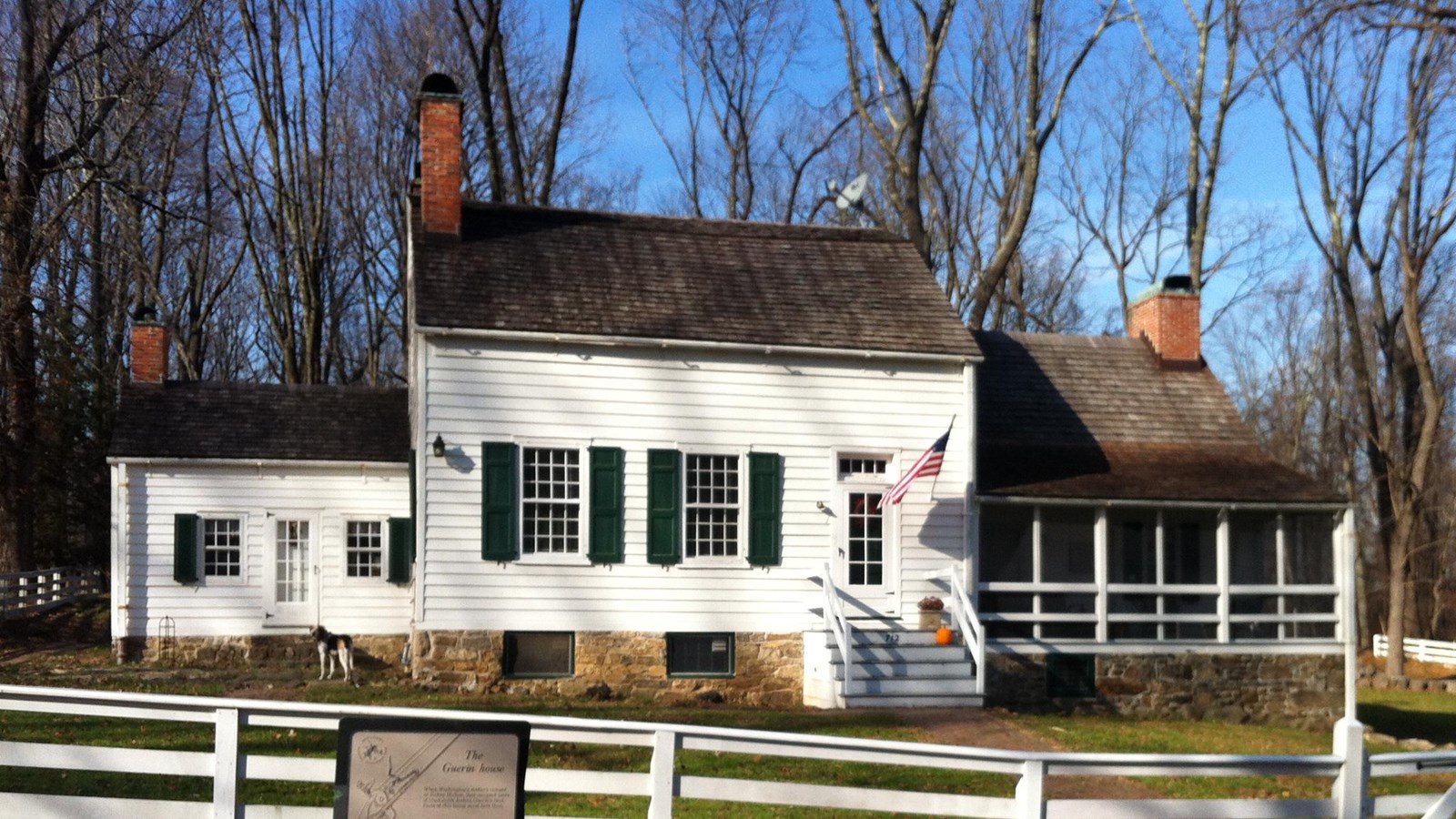 A colonial style farmhouse with white fence and wayside explainer near a roadway.