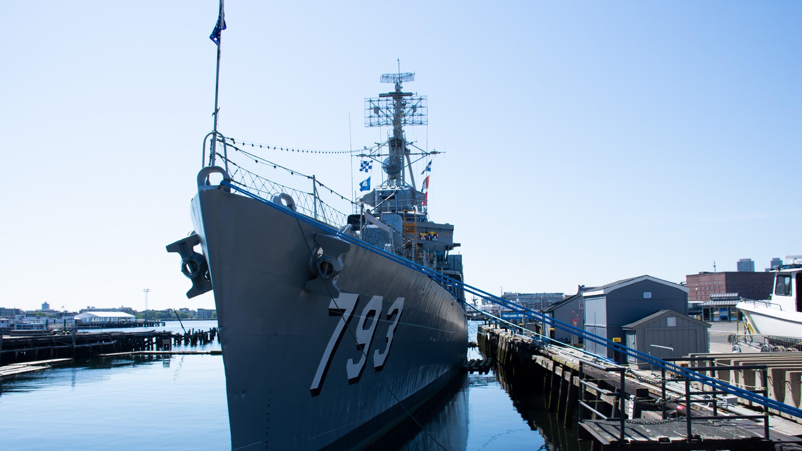 Grey steel hulled ship moored to a pier on the right, Block letters on bow read 793