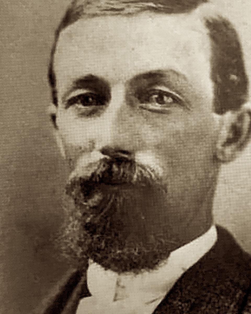 A sepia portrait photo from the 1800s depicts a bearded man in a white collar and dark jacket.