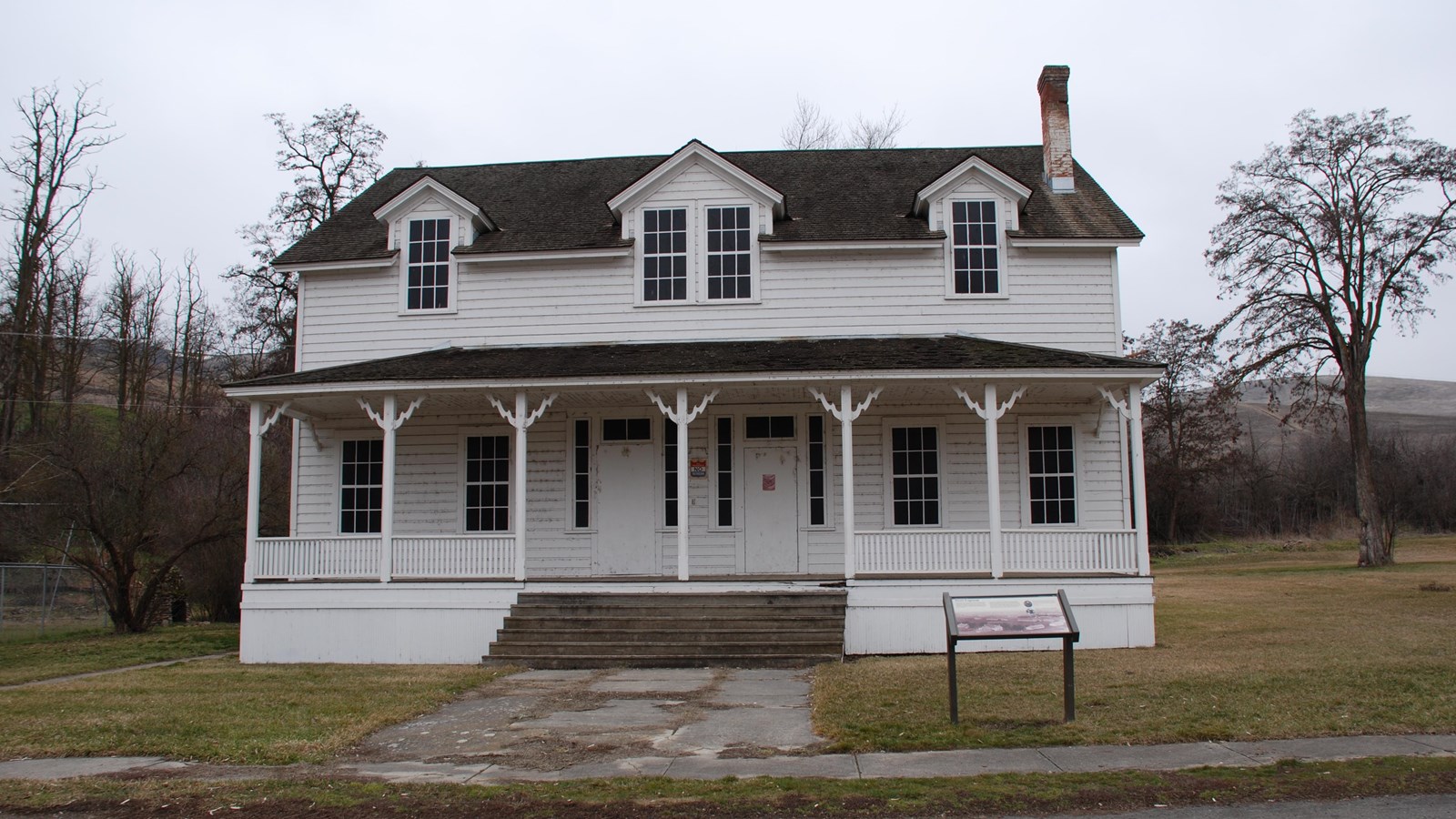 A two-story white wooden building. It has a covered porch and sign in front