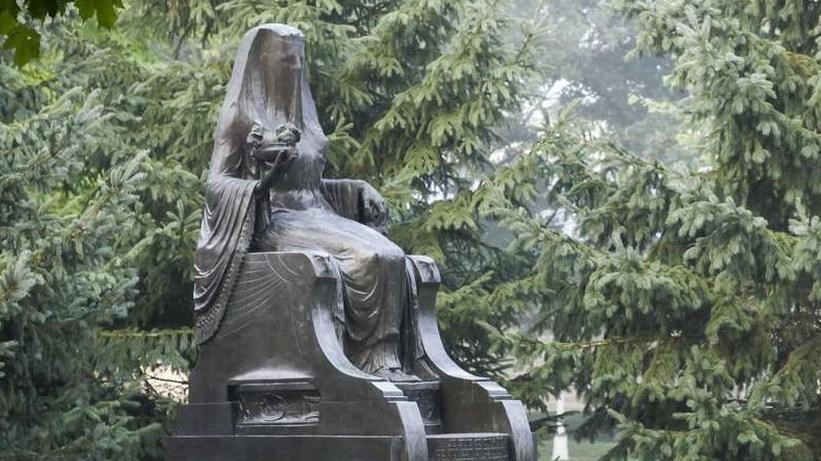 A bronze statue of an Egyptian goddess sits along a park path in the morning fog.