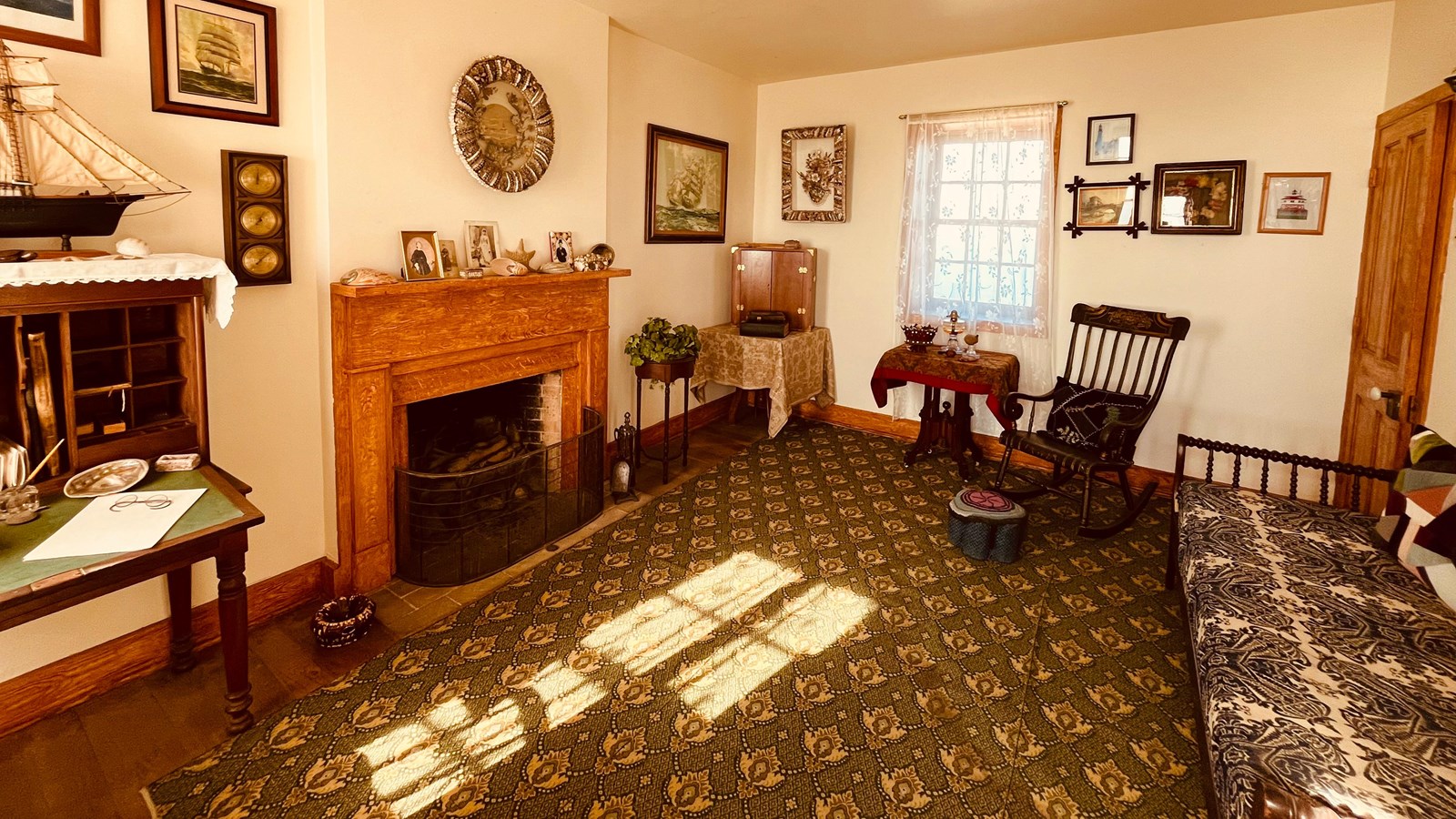 A room with a rocking chair, couch, fireplace, and table, decorated with framed paintings.