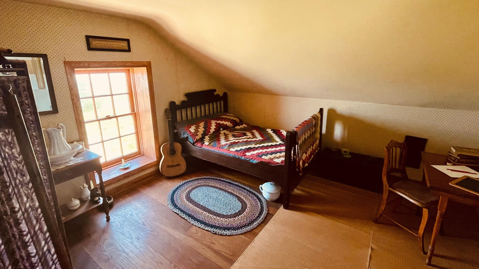 A bedroom with a small bed, window, small rug, and a table. 