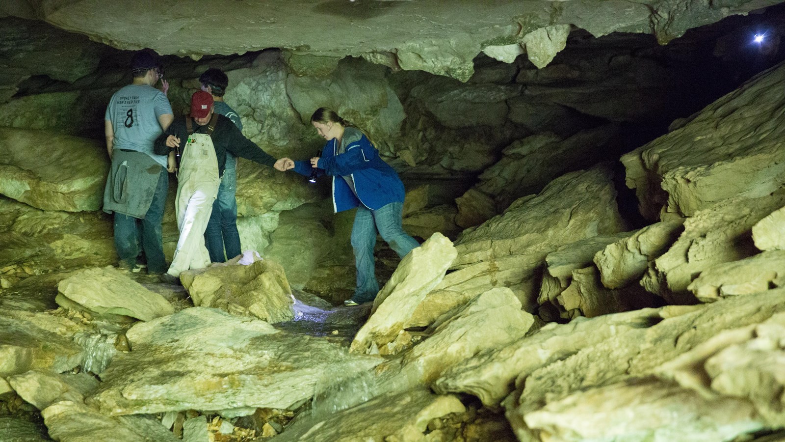 Cavers entering and exiting Eden Falls Cave. A flashlight shines toward us from a dark passage.