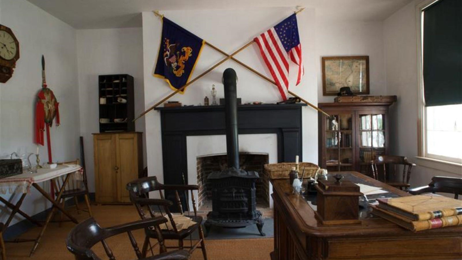 A white painted room with wood floors. A fireplace in middle of the room with two flags .