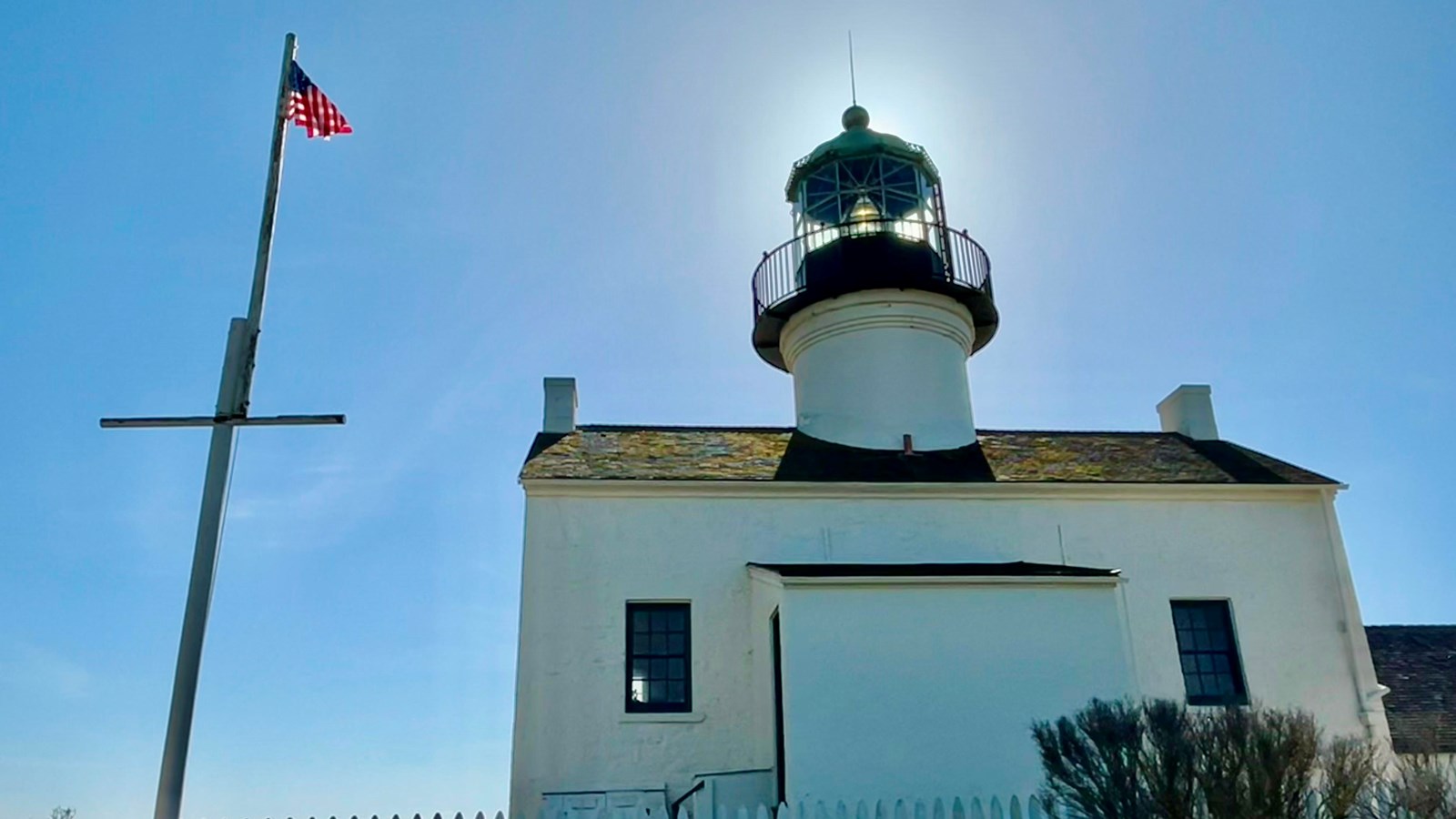 A white lighthouse with a tall flagpole flying the American flag. 