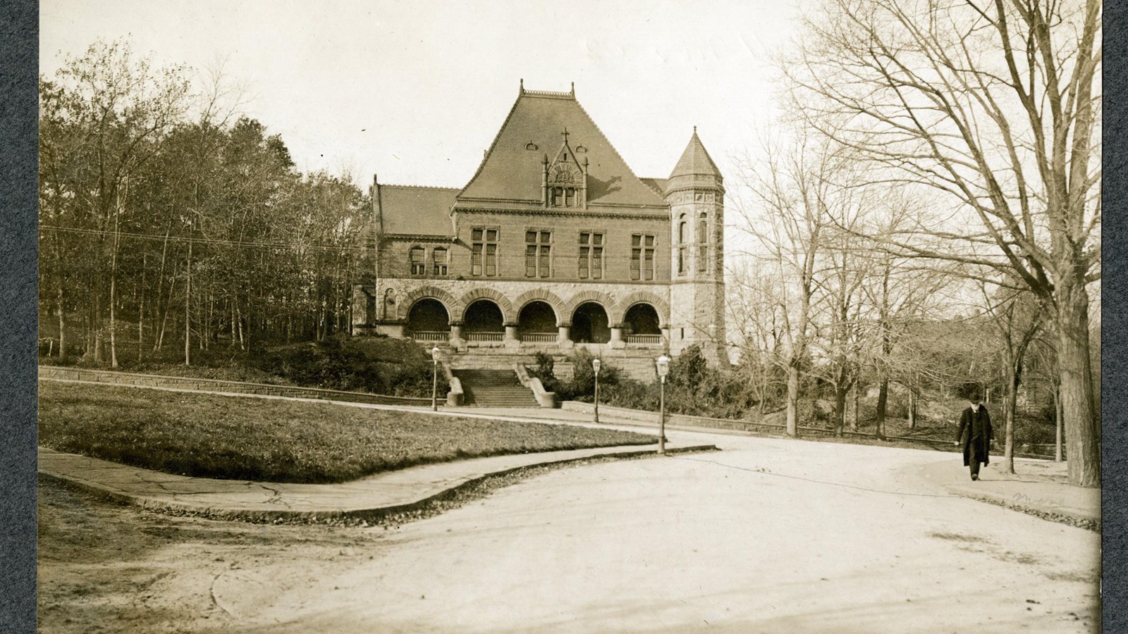Black and white of large stone building on hill with trees on both side of buidling