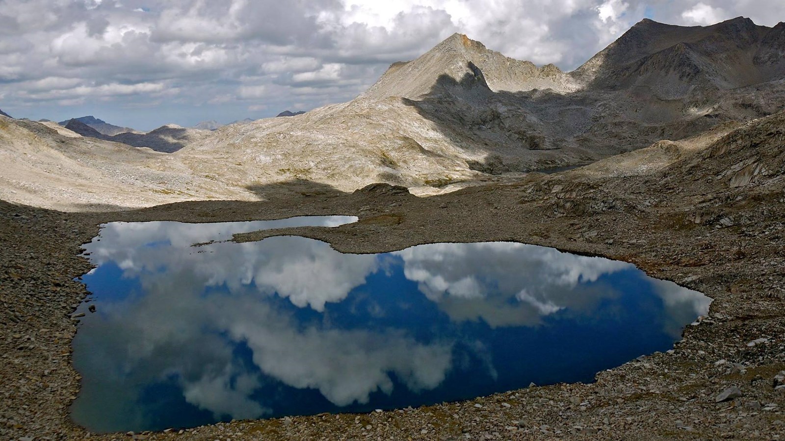 Clouds reflect off a blue alpine lake nestled in high sierra peaks of Kings Canyon.