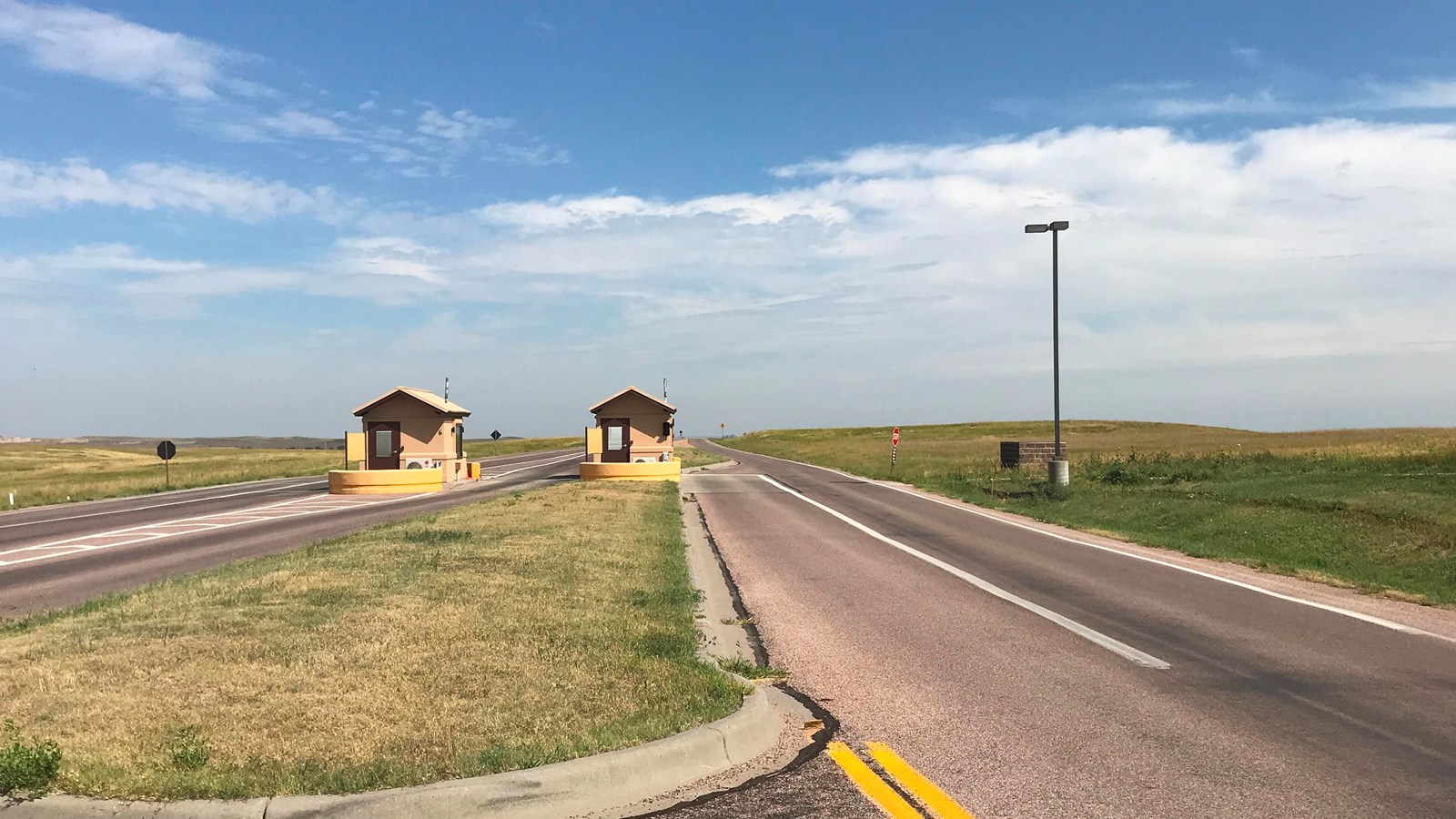 Two tan buildings in the middle of paved road under blue sky.