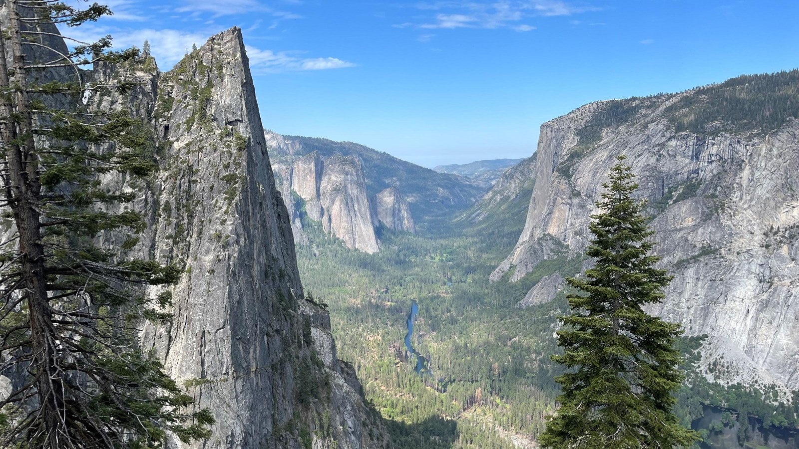 Towering cliffs frame a deep valley with vibrant grasses and a blue river on the valley floor