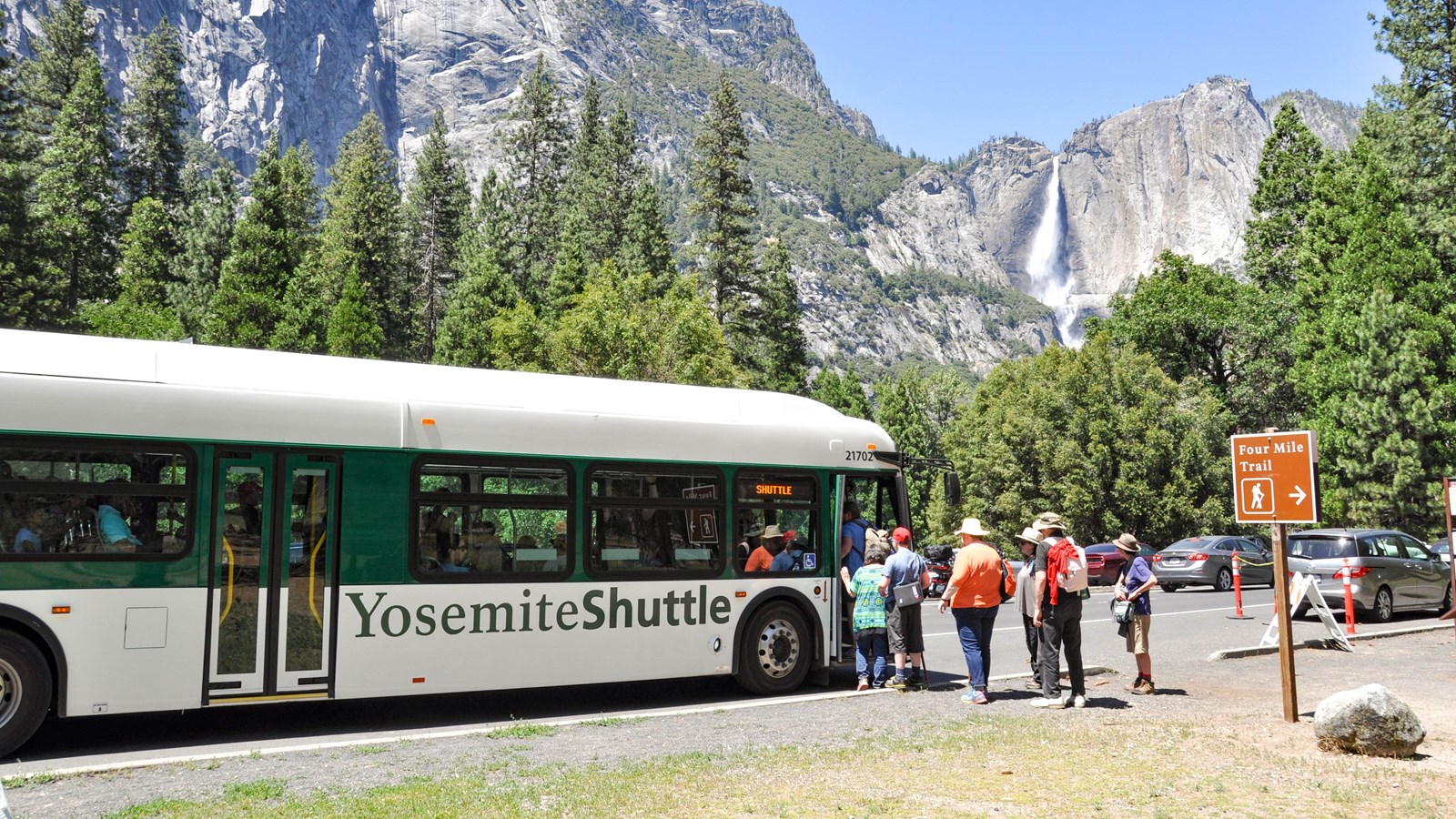 People boarding shuttle bus at Four Mile Trailhead with Yosemite Falls in the background.