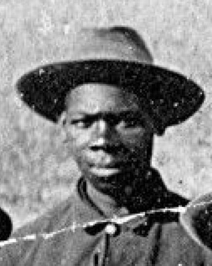 Black and white photo of African American man in 1870s Army coat and hat. He is looking forward.