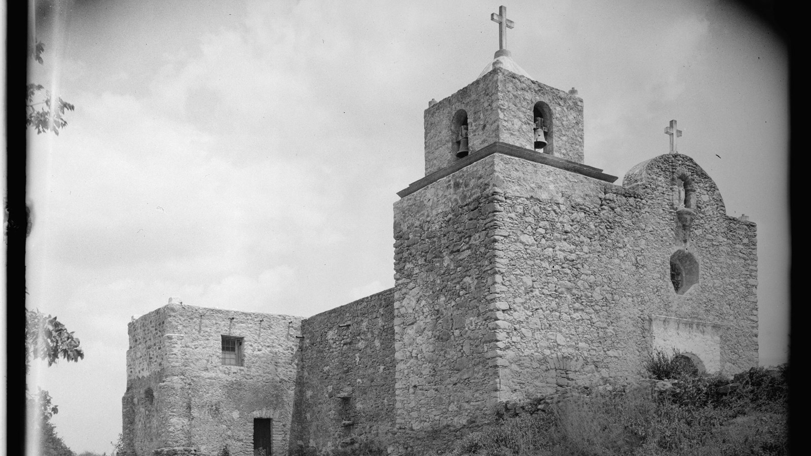A black and white photo of a stone building with two crosses on top and a bell tower.