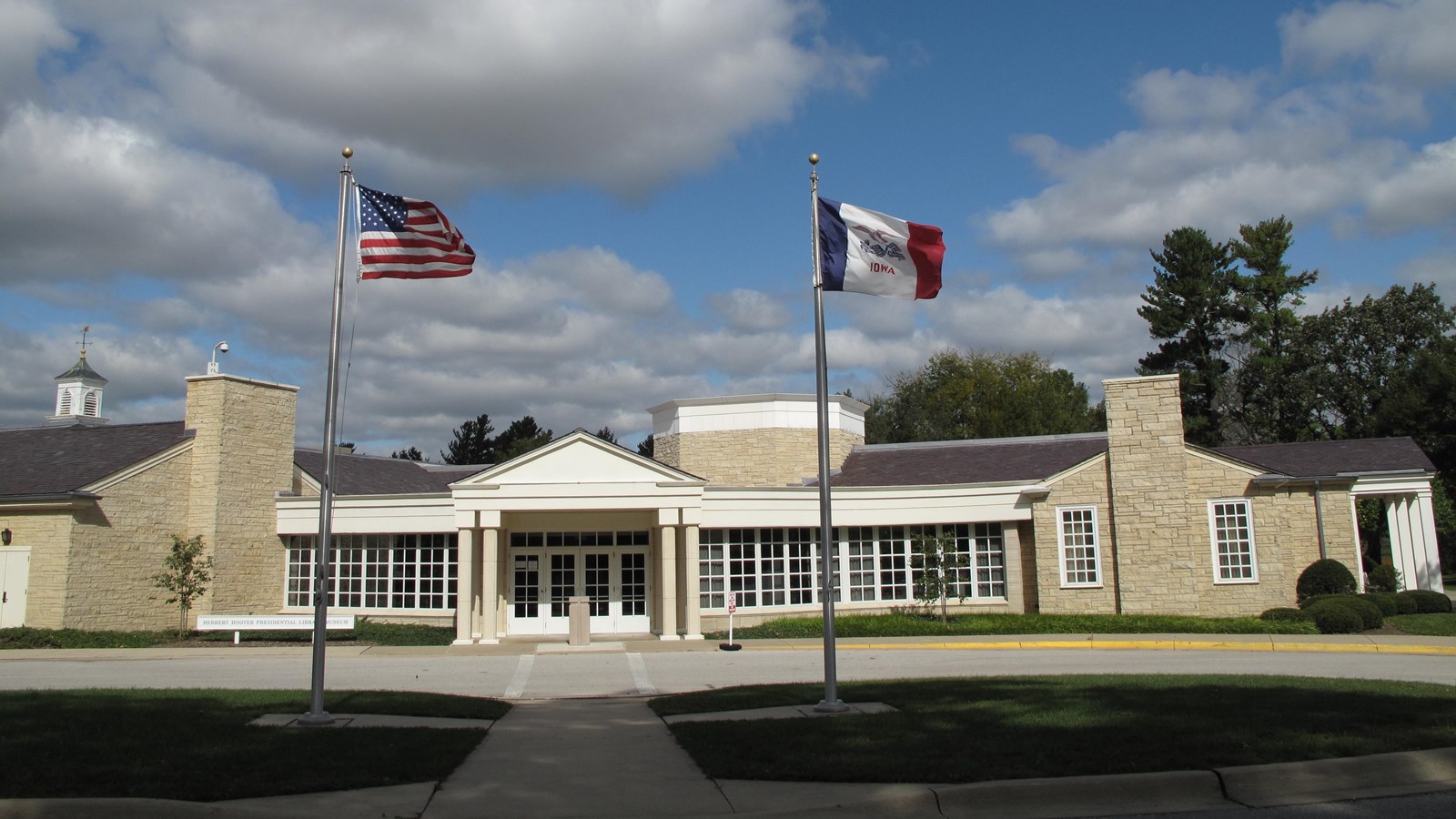 Flags fly in front of a public building of rough-faced yellowish stone and a white portico.