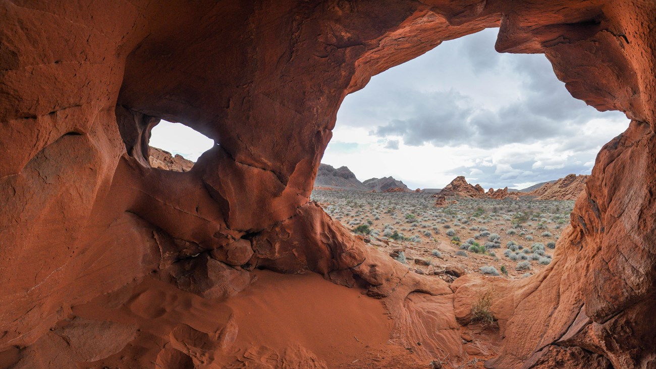 Looking out of a cave in a rock formation out into a desert landscape.