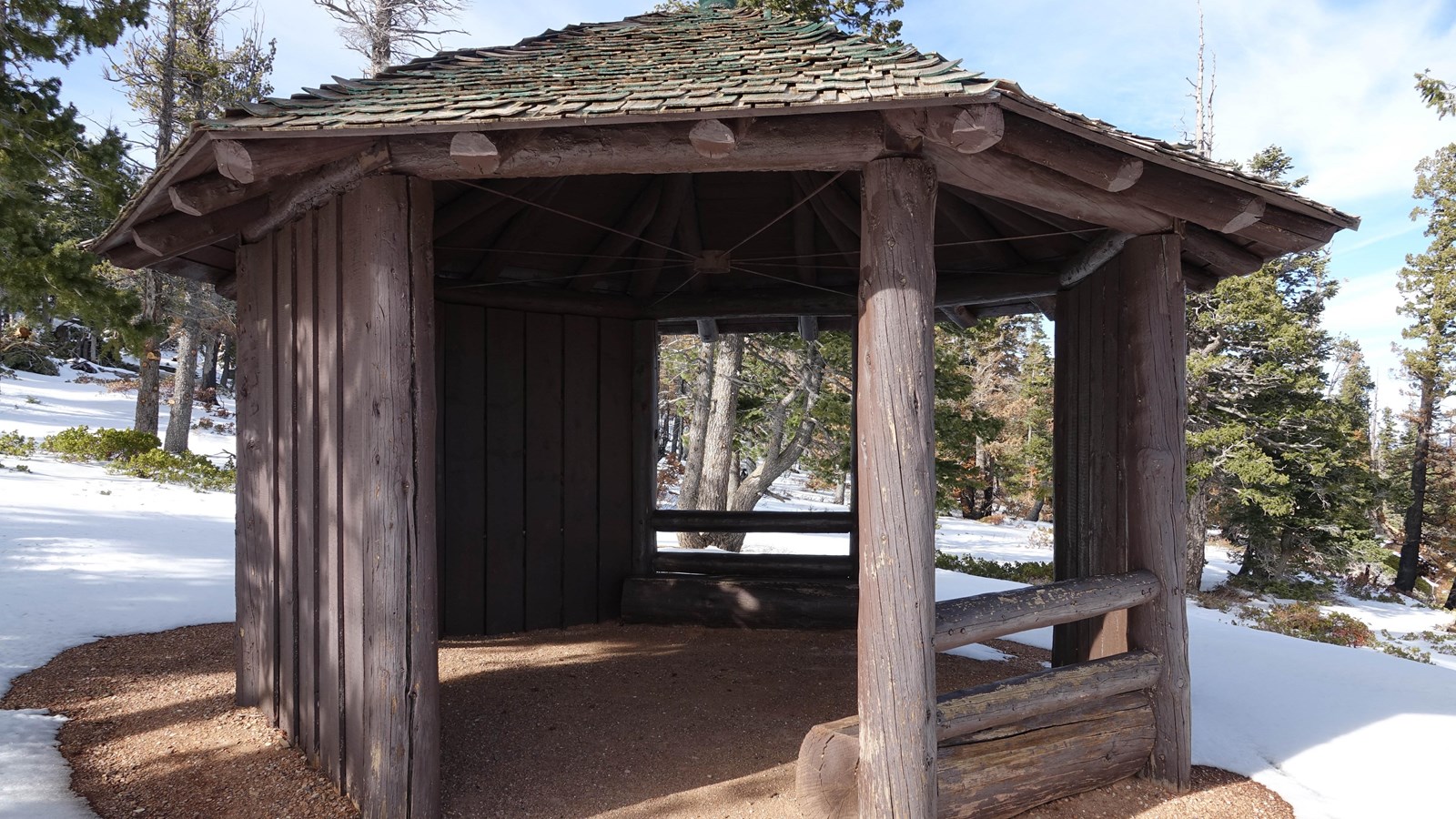 Wooden gazebo with green wooden shingle roof in snowy forest
