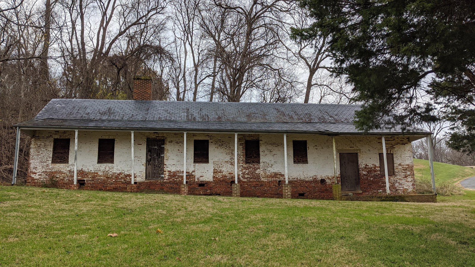 A one story brick building with white-washed walls, black shingled roof, and columns