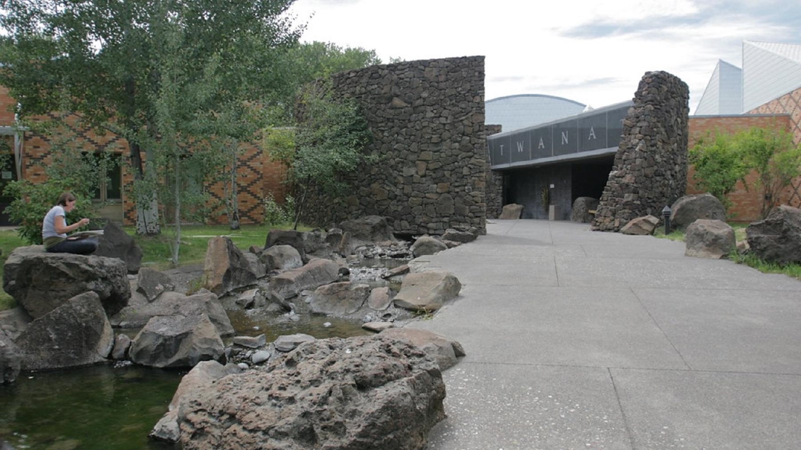 A paved walkway passes by a rock-lined pond as it leads to the museum entrance