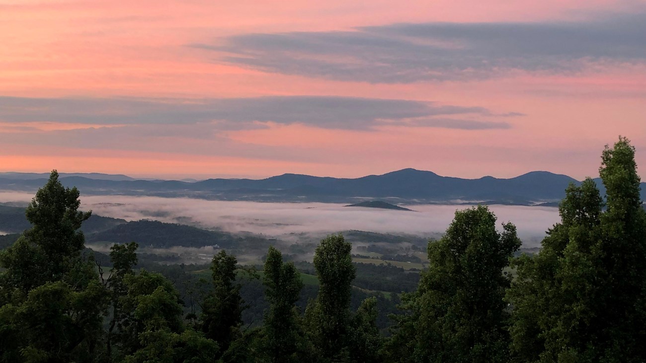 Image of a colorful sunrise viewed from Afton Overlook.  Low clouds hang over the valley below.