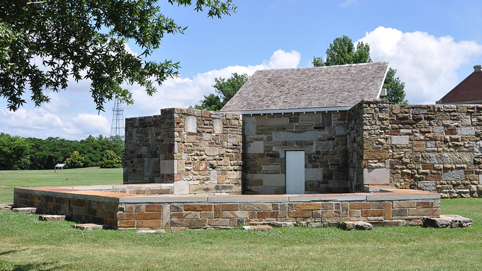 Low pentagon shaped stone wall connects to a 10 foot stone wall with a white door in center.