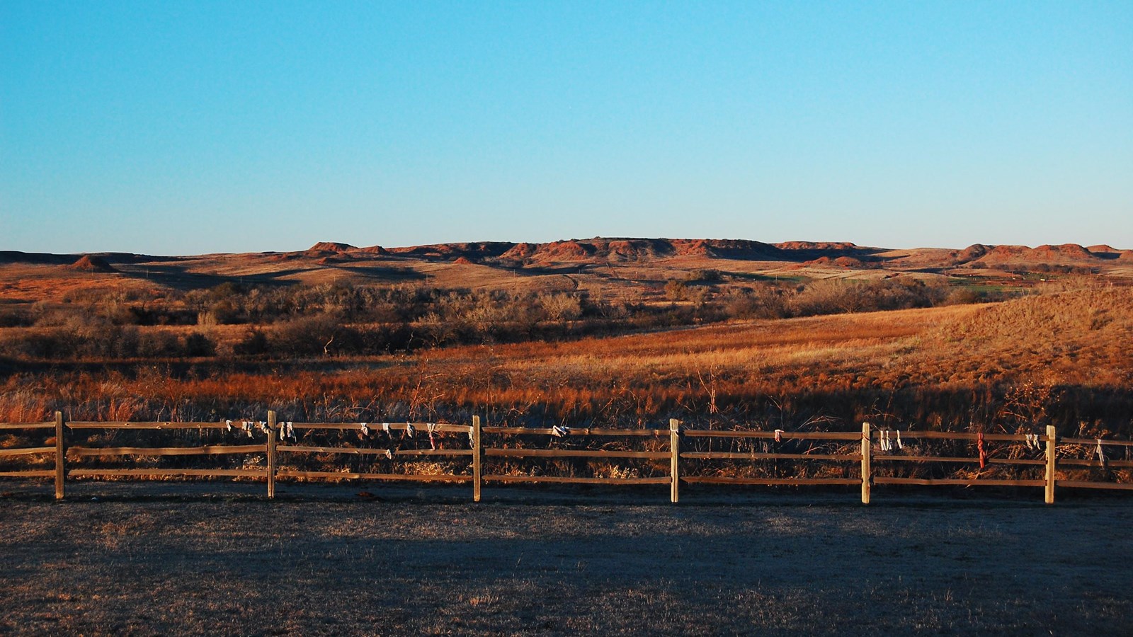 A wooden fence with ribbons tied to it in front of a grassy valley with hills in the distance.