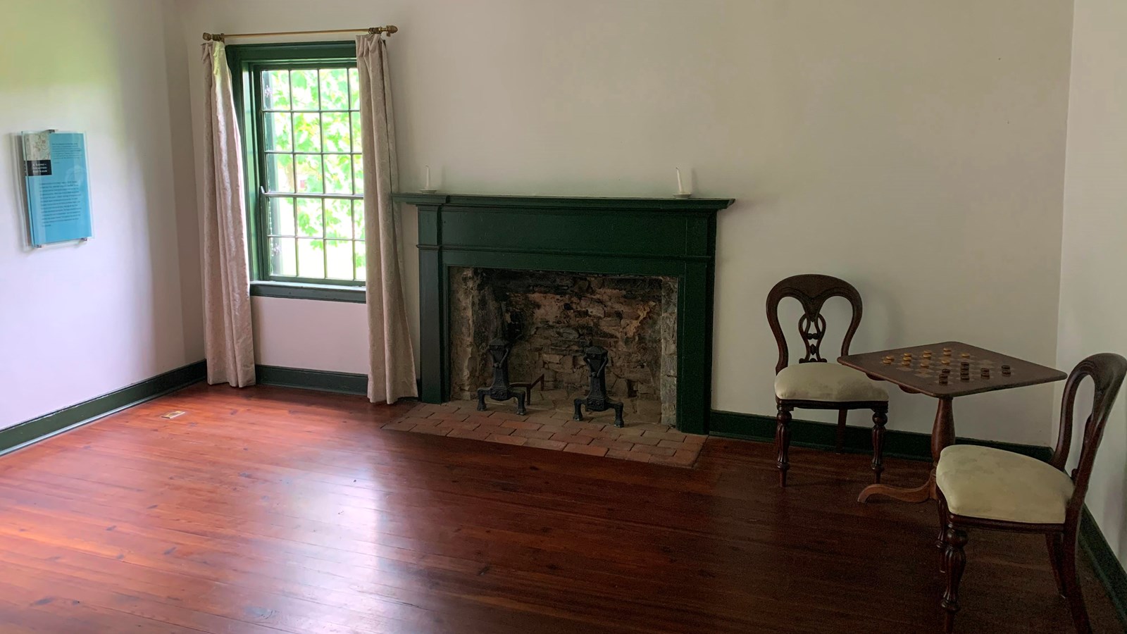 Two chairs sit at a table with checkers on it. Next to the table is a window and fireplace.
