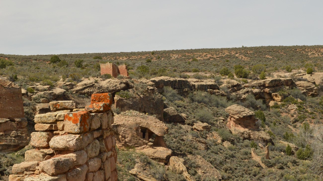 a crumbling stone wall in the foreground, with other stone structures across the canyon.