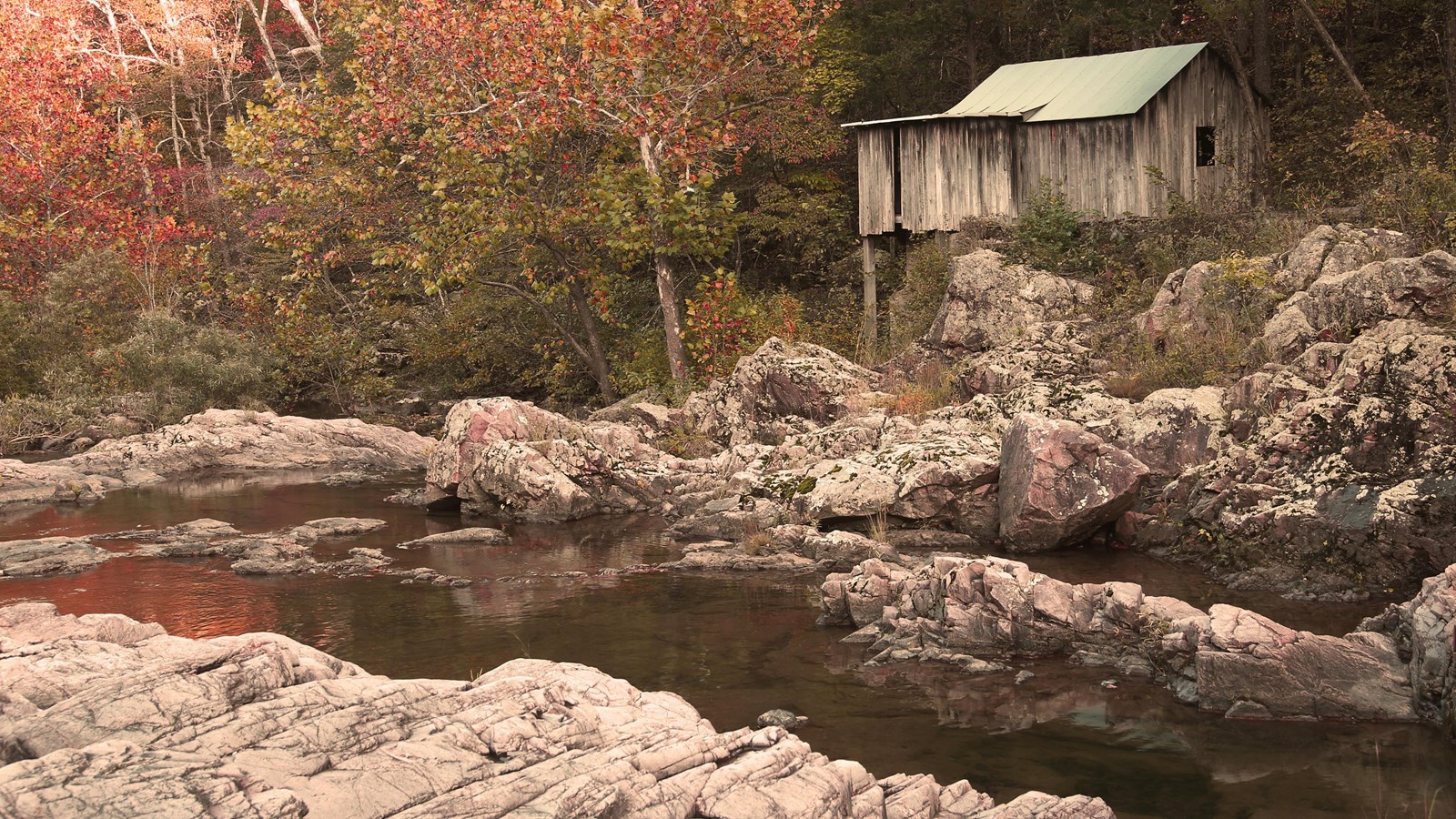 purple grey rocks with a stream flowing between, a wooden building sits up above with a tin roof