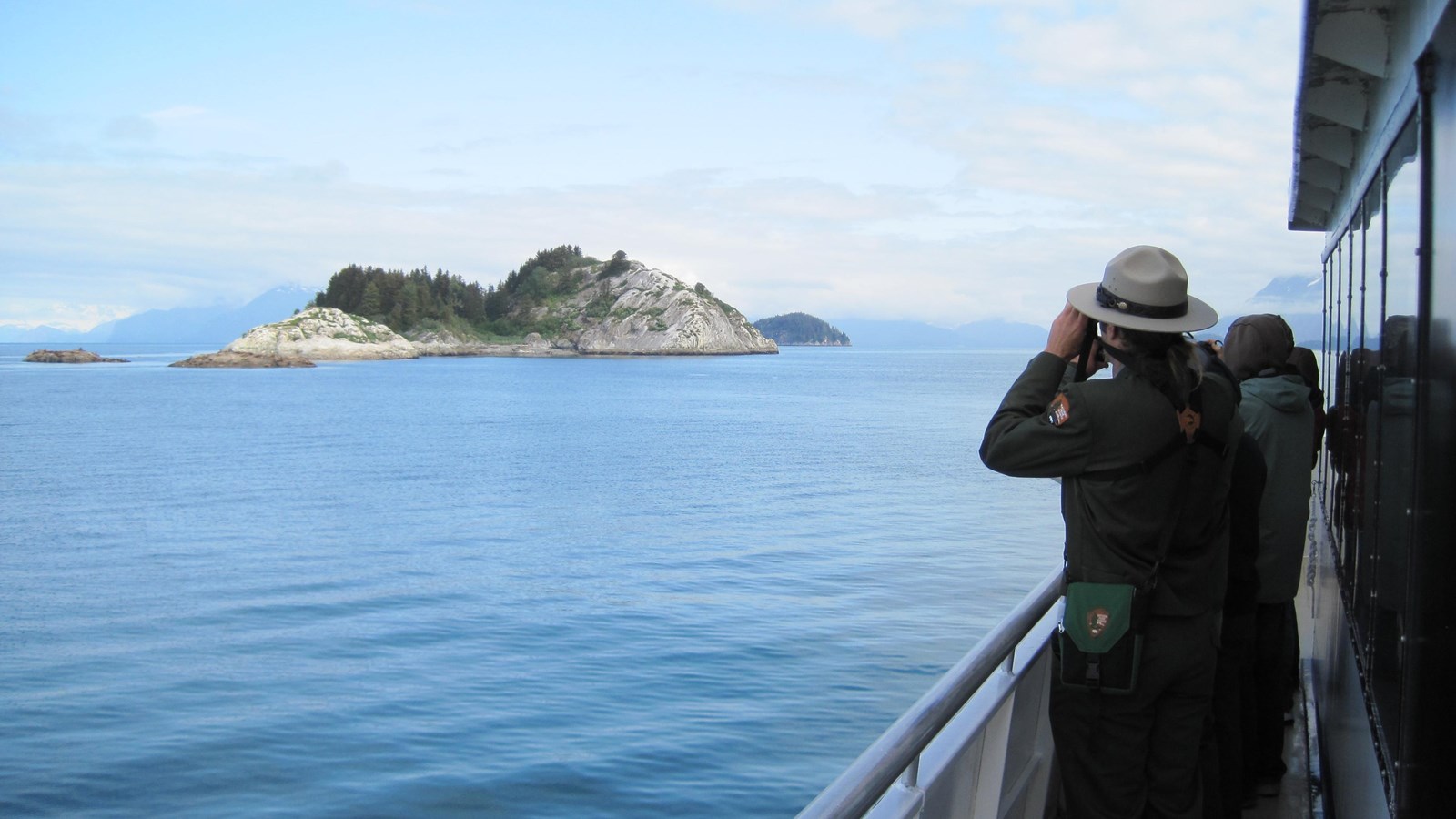 A park ranger aboard a tour boat points their binoculars towards South Marble Island.