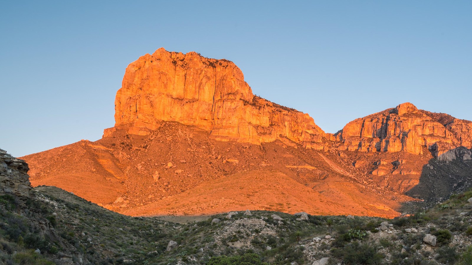 A tall peak is lit by the rising sun. 