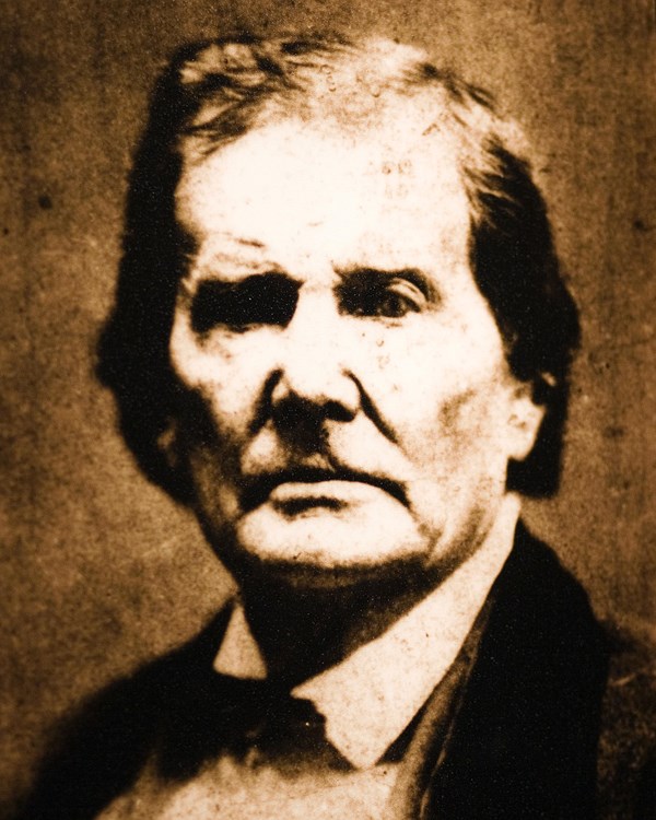 Sepia portrait of a man with a very serious look and a high forehead and sunken, dark eyes. 