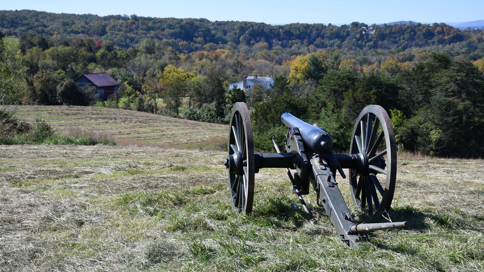 Cannon on a grassy knoll overlooking fall foliage and a historic farm. 