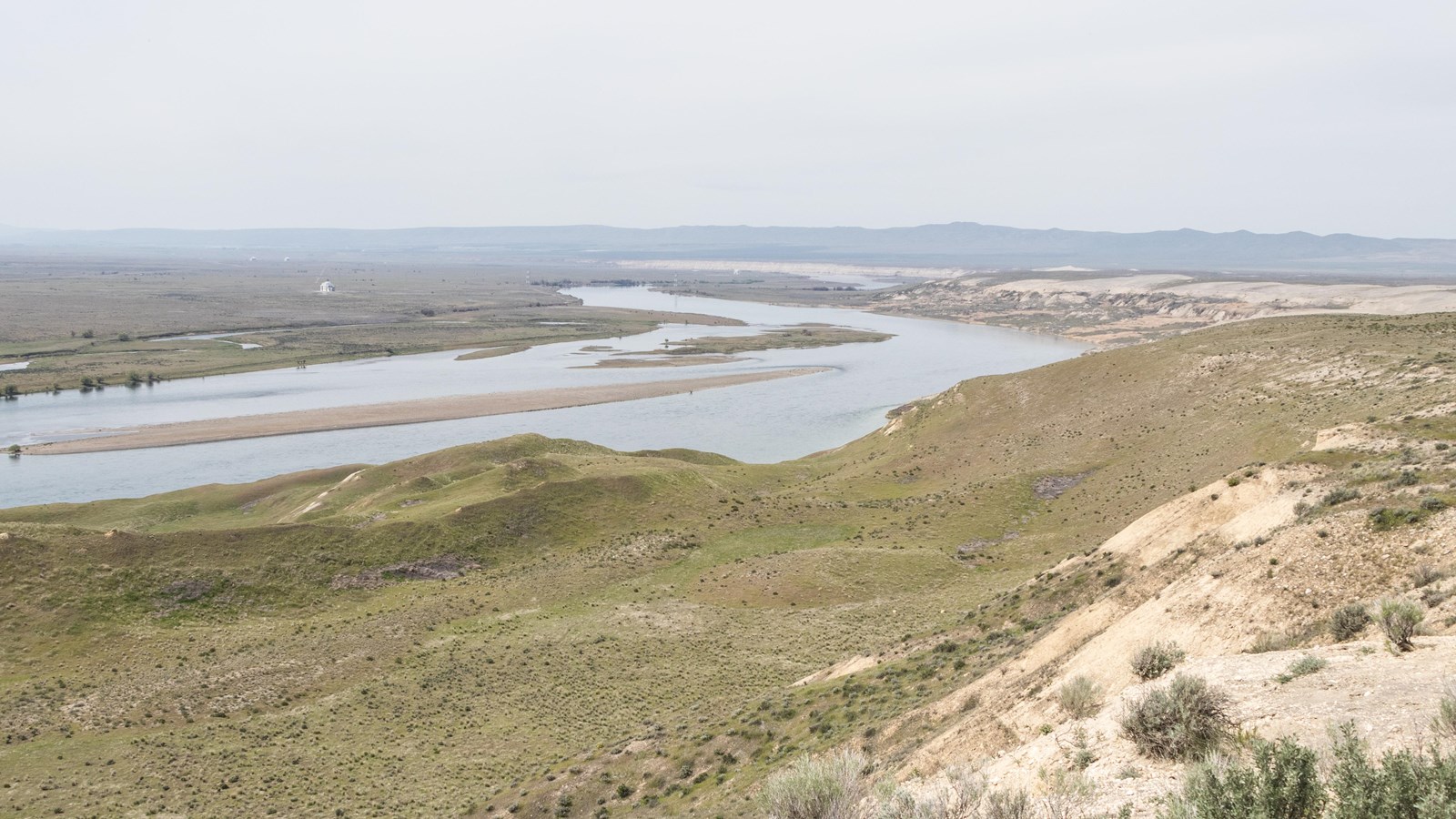 Color photograph of the crest of a desert hill looking down and across a large river