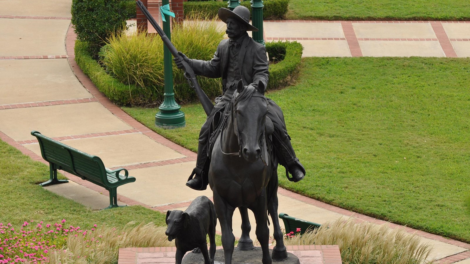 View from above of a bronze statue of a man on a horse holding a rifle with a dog next to it.