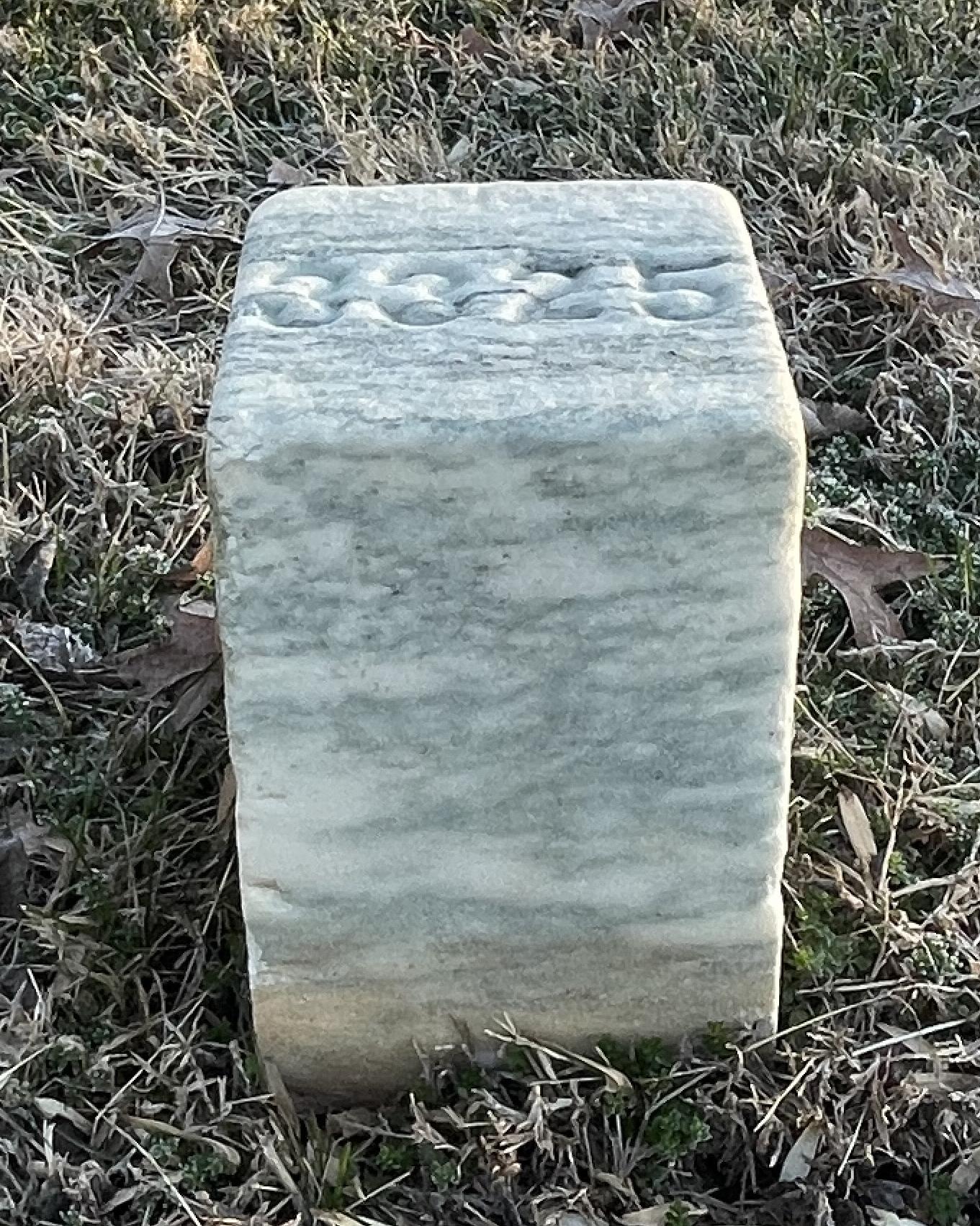 Short, square headstone with a number on the top. 