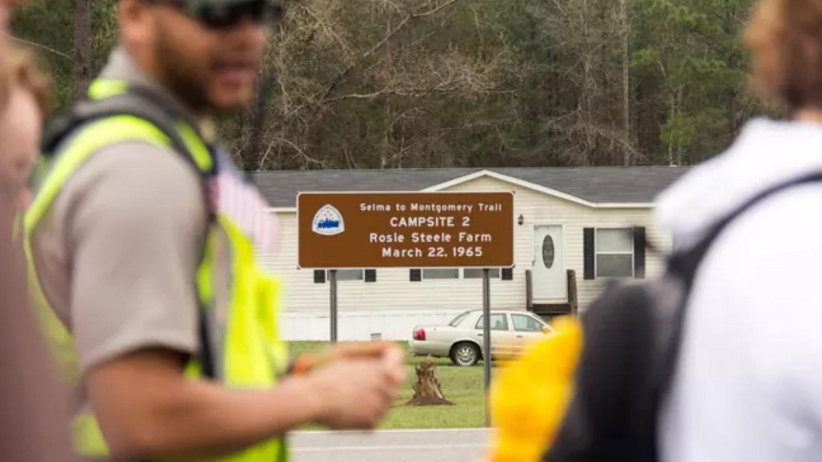 A large brown sign in a front yard along a highway.