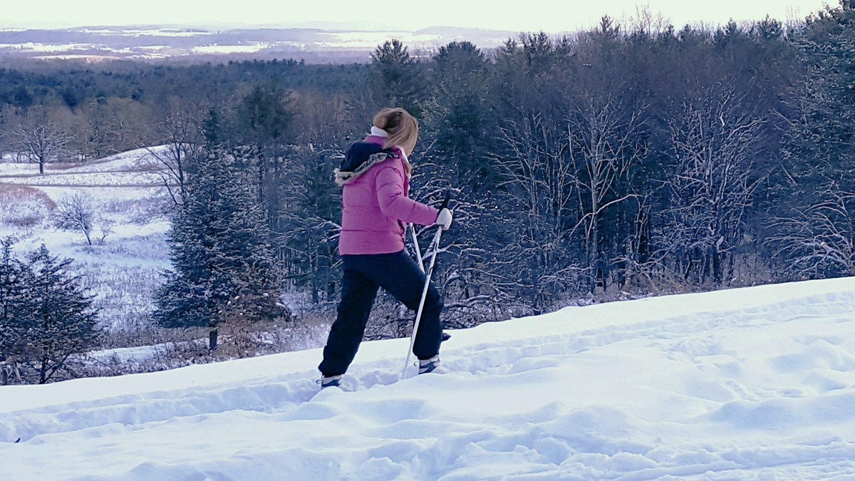 Woman in pink jacket on skis. Open vista overlooking the battlefields form backdrop. 
