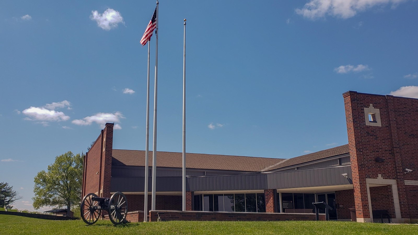 A road leading up to a large brick building at the top of a hill. The sky is blue with clouds.