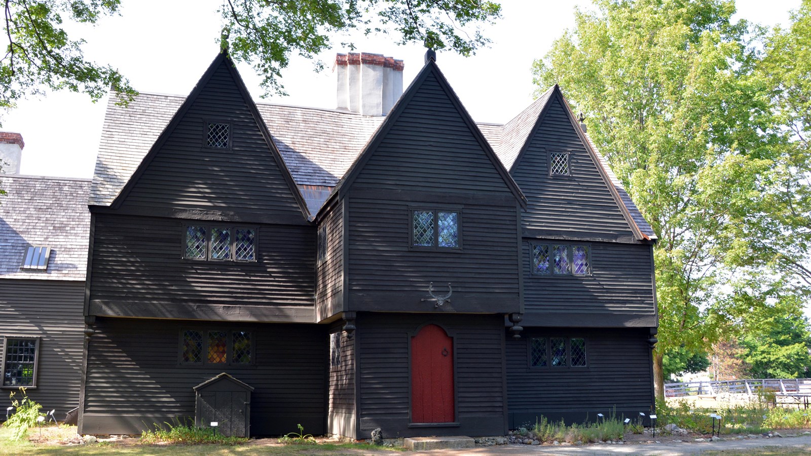 Gray three-story house with red door in center, three roof peaks in a row, and stained glass windows