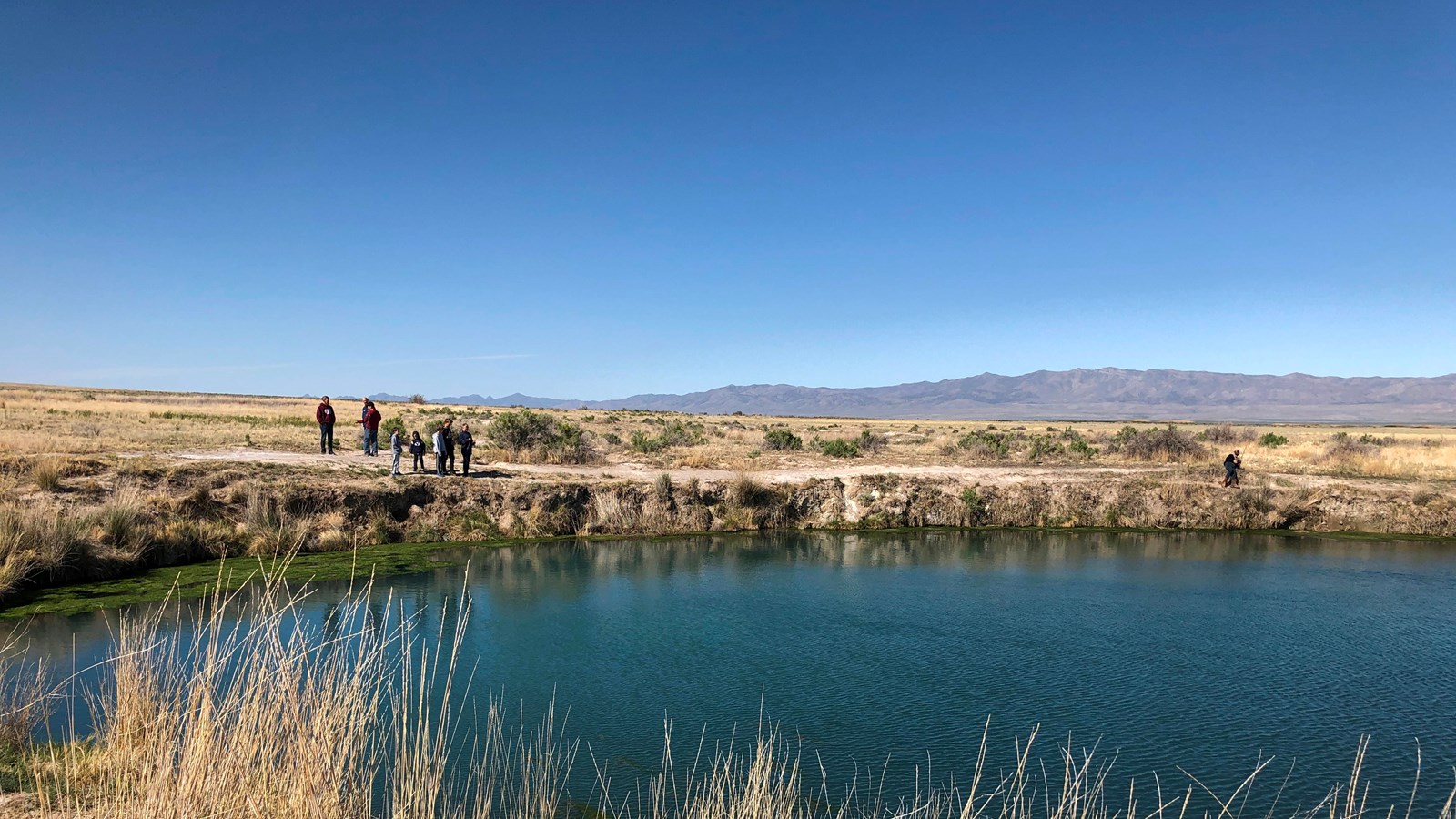 A still blue pond surrounded by a desert landscape.