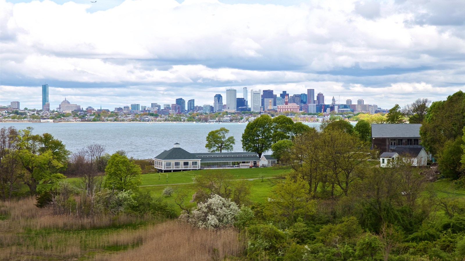 Thompson Island, with green grass field with buildings in the foreground and Boston city line behind